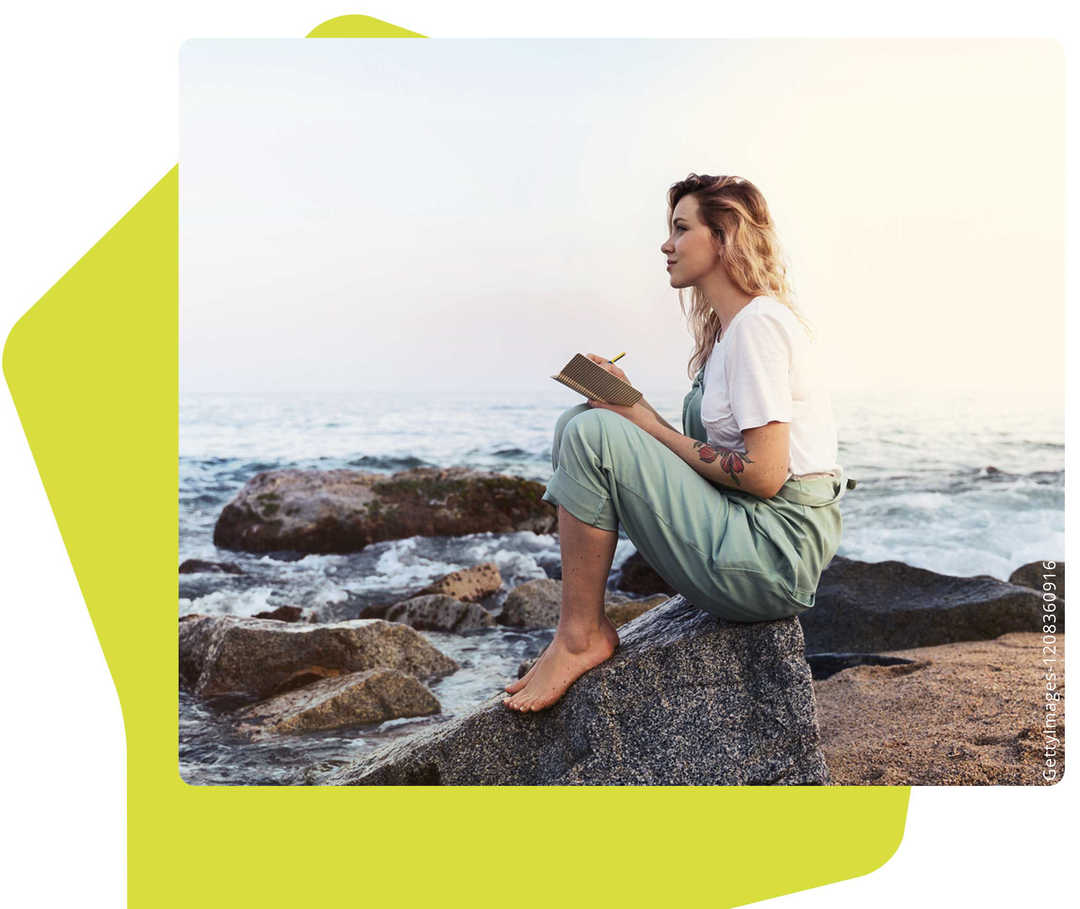 Das Bild zeigt eine Frau auf einem Felsen am Strand Das Bild zeigt eine Frau auf einem Felsen am Strand